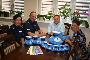 Komendant Powiatowy Policji w Lipnie wraz ze starostą lipnowskim siedzą przy stole na którym leżą &quot;Polfinki&quot;maskotki kujawsko-pomorskiej policji