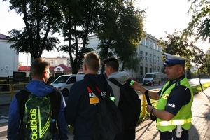 policjant ruchu drogowego nakłada 3 uczniom odblaski na plecaki