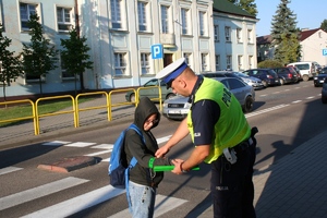 policjant nakłada chłopcu na rękę opaskę odblaskową