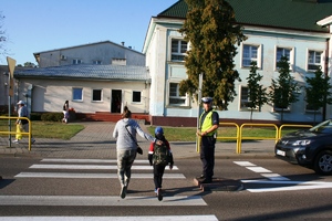 policjant wstrzymuje ruch pojazdów, aby dzieci mogły przejść na drugą stronę jezdni