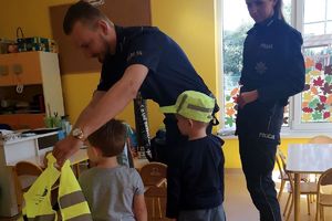 policjant ubiera dziecku kamizelkę odblaskową