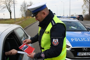 policjant ruchu drogowego wręcza kierowcy ulotkę profilaktyczną